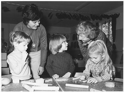 Black and white photograph of Lady Plowden (right) with 3 school children (middle) and their teacher (left) taken whilst visiting a primary school