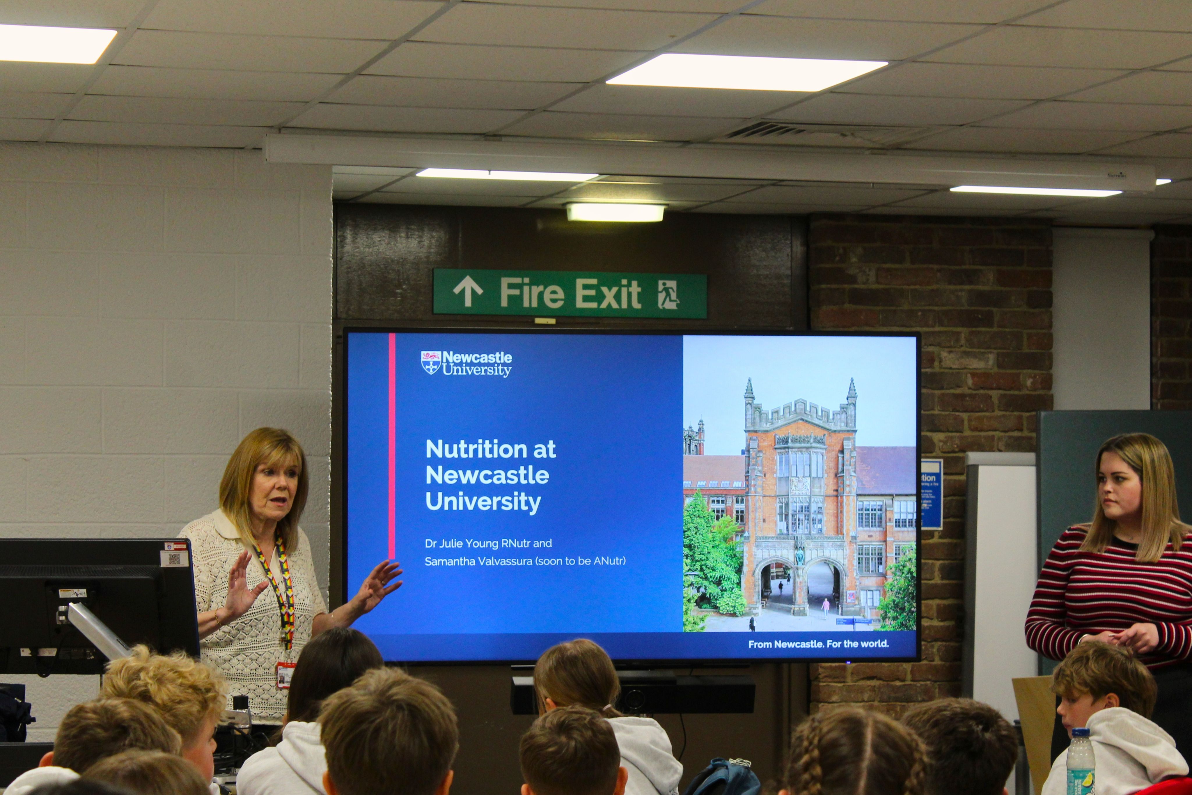 A lecturer standing in front of a screen speaking