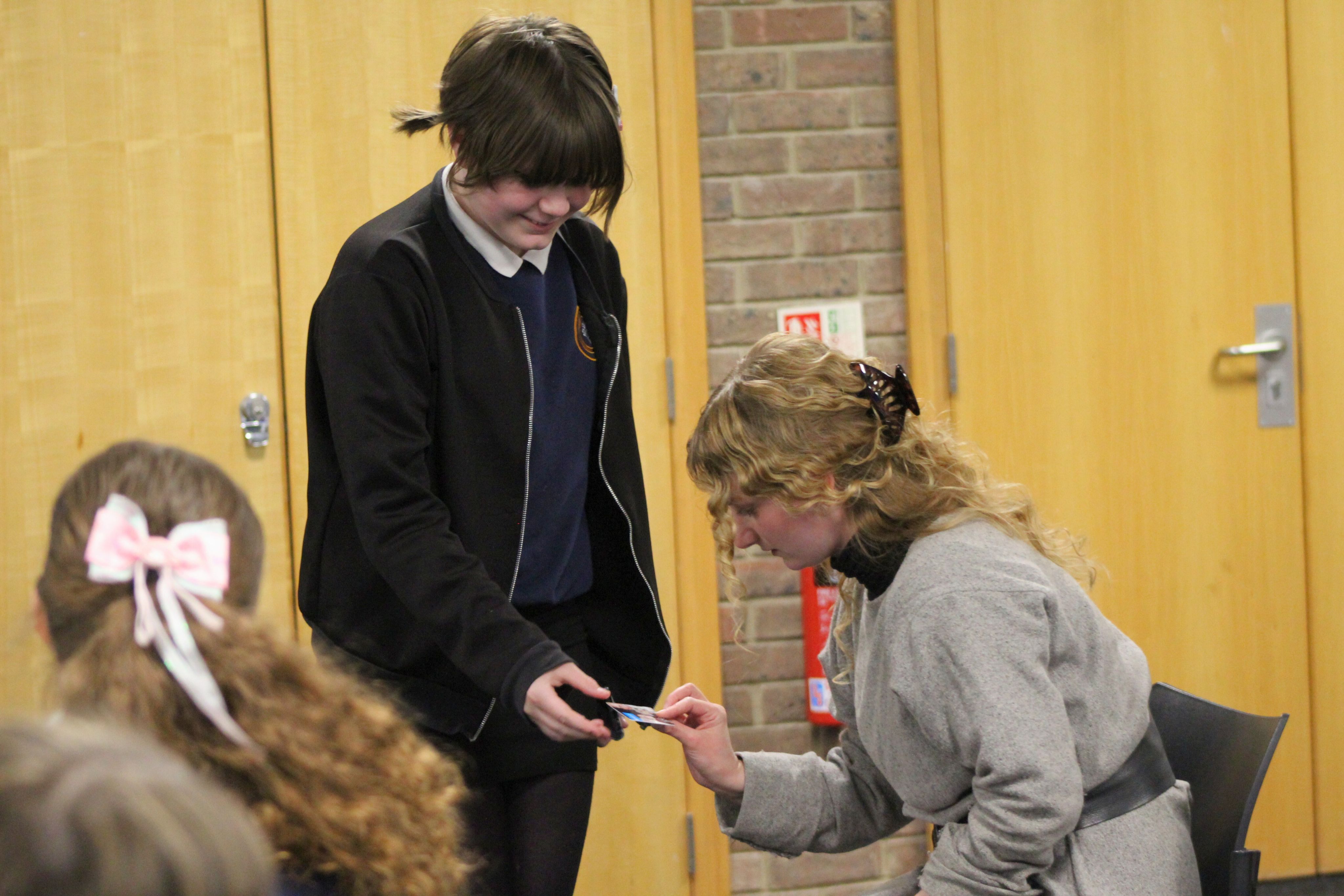A person holding a credit card out to an actress dressed in grey prison costume