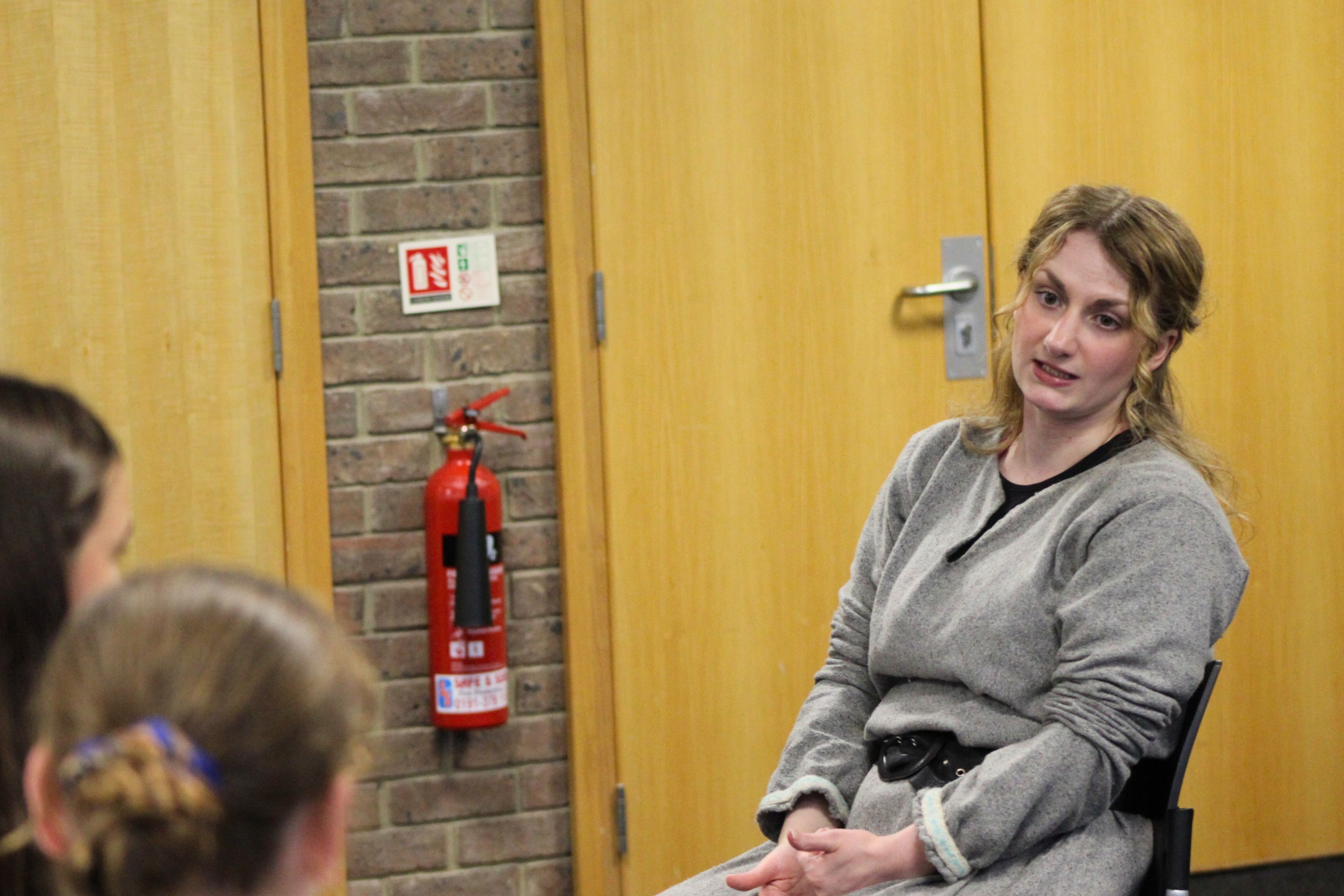 An actress dressed in grey prison costume talking to children