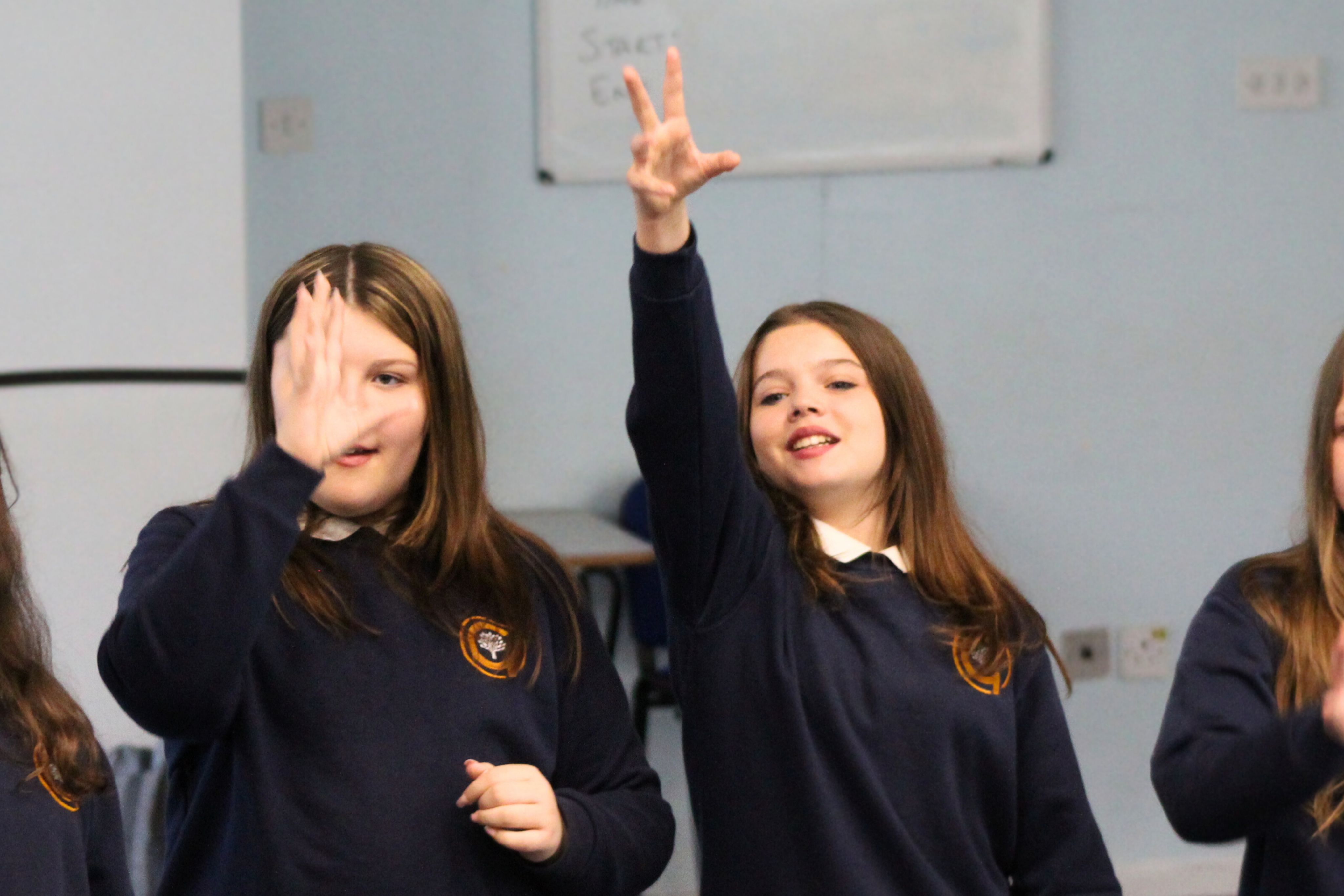 Two students with their hand raised during a drama activity