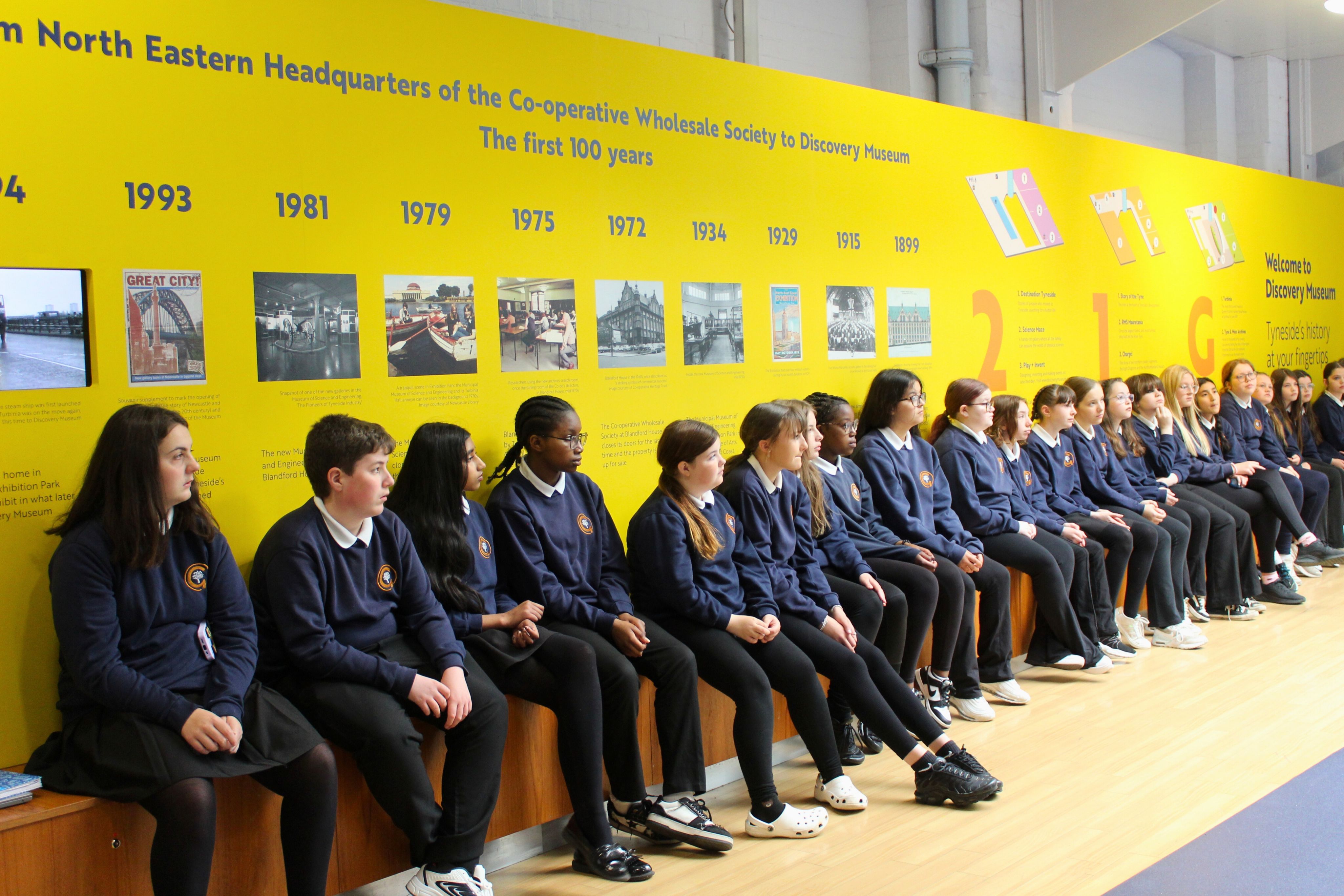 Students sitting in a line along a bench