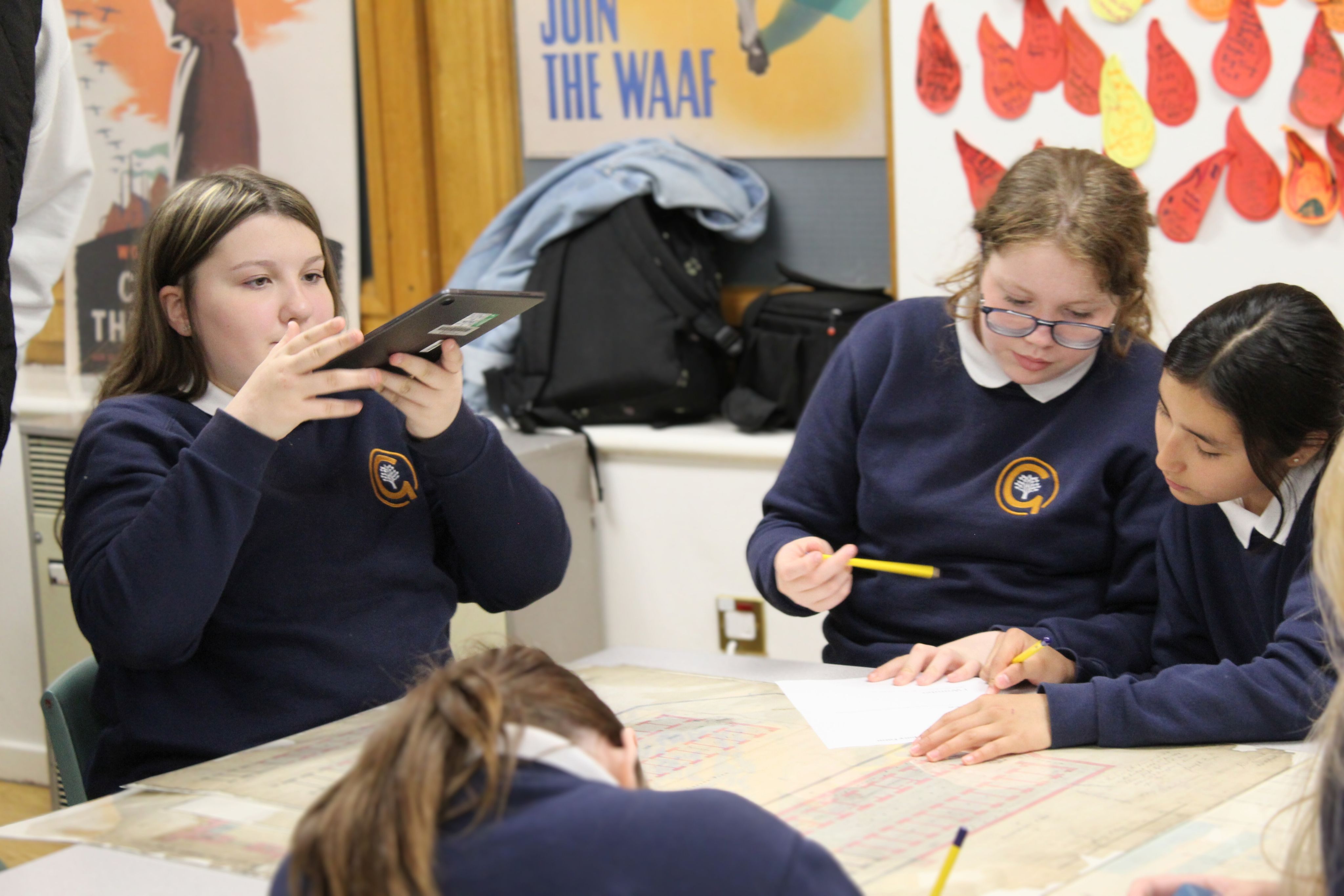 A student holding a tablet on the left, and a student holding a pencil on the right.
