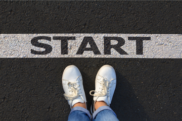 Two feet in white trainers stand on tarmac behind a line that says 'START'