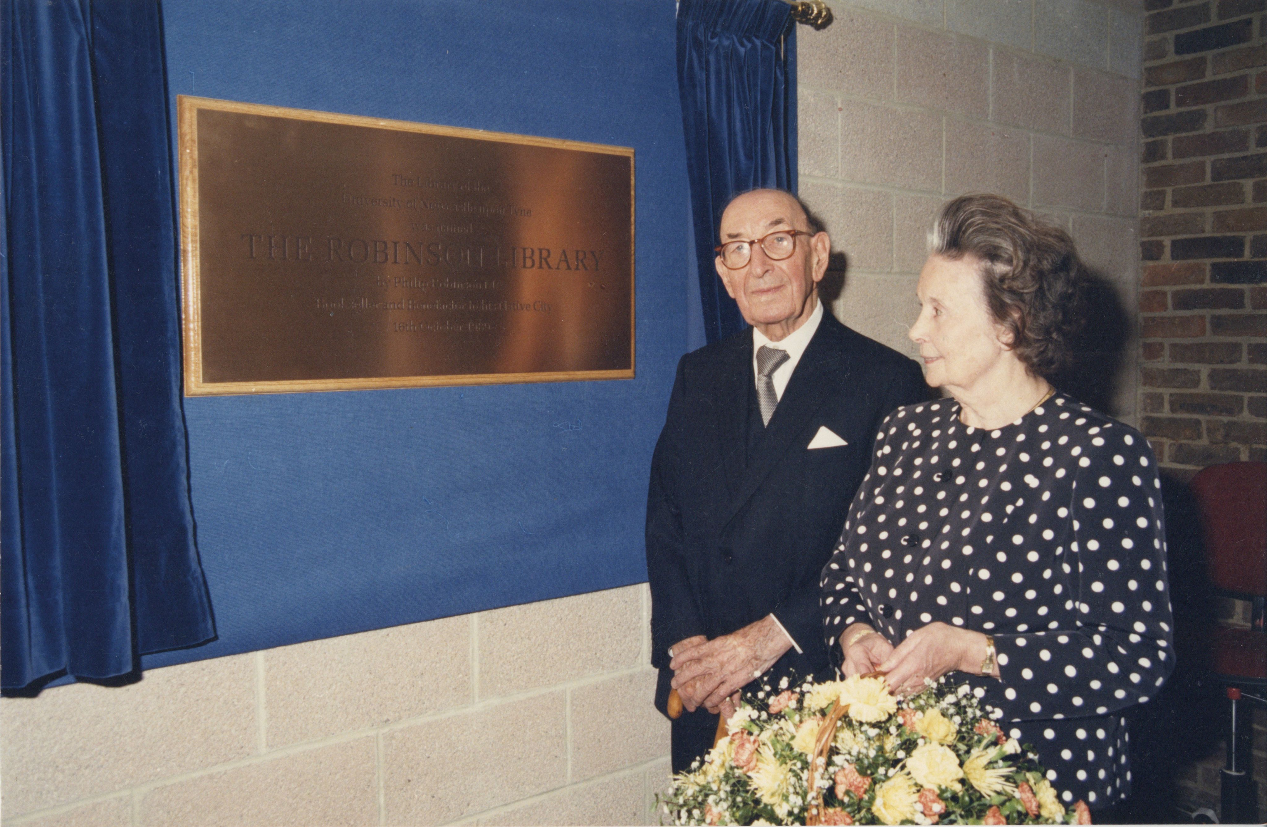 A man and a woman stood in front of a brass plaque.