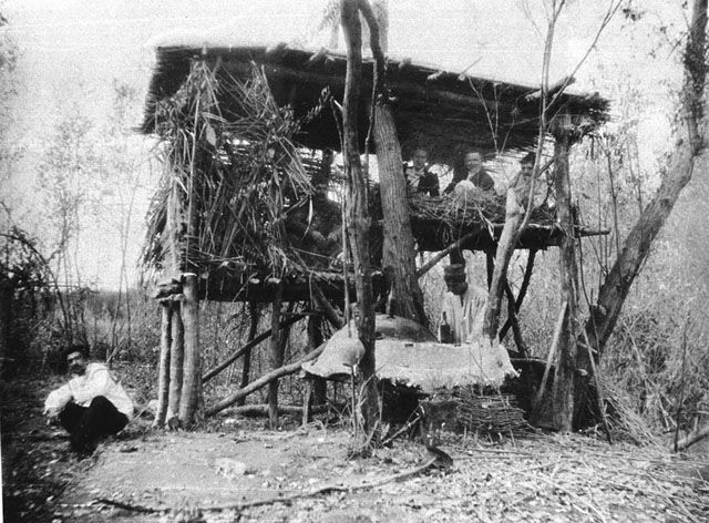 Photograph of villagers and Europeans in an elevated hut.